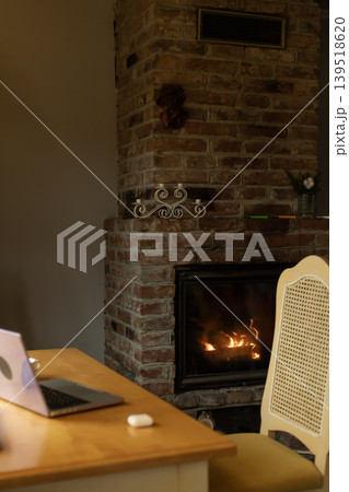 Fireplace with Burning Fire Laptop and Desk in Warm Lit Home Interior 139518620