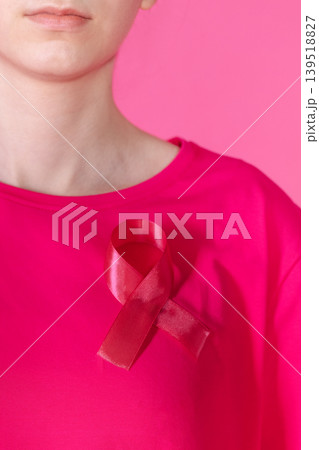 Close-up of a pink satin ribbon as a symbol of the fight against cancer on a woman T-shirt. A girl in pink clothes on a pink background with a ribbon. 139518827