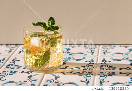 Close-up of a glass of mineral water with lemon and fresh mint and ice cubes on a table made of white tiles with blue patterns. A cup of cool, delicious, healthy drink. 139518830