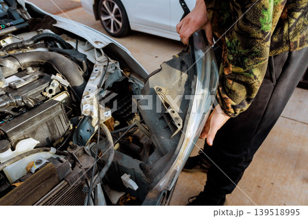 Worker works on fixing car headlight during garage service Worker works on fixing car headlight during garage service 139518995