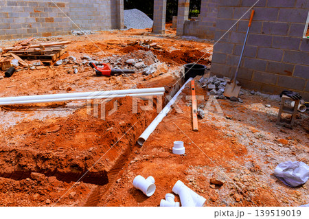 Construction site dug trench with pipes, tools on red soil landscape during waste utility system Construction site dug trench with pipes, tools on red soil landscape during waste utility system 139519019