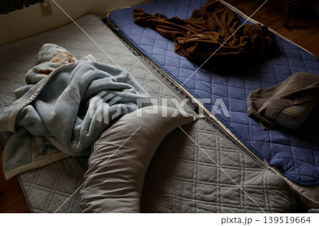 薄暗い部屋に敷きっぱなしの枕と布団。寝具の放置と生活感。 薄暗い部屋に敷きっぱなしの枕と布団。寝具の放置と生活感。 139519664
