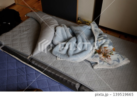 薄暗い部屋に敷きっぱなしで放置された枕と布団。灰色の寝具 薄暗い部屋に敷きっぱなしで放置された枕と布団。灰色の寝具 139519665
