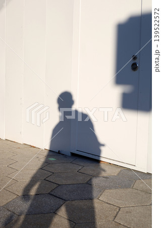 Shadow of person walking beside white wall 139522572