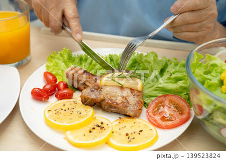 Asian elderly woman patient eating pork chop stake and vegetable salad for healthy food in hospital. 139523824