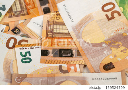 Crisp scattered fifty euro banknotes layered for wealth illustration, warm tones, closeup macro of paper texture and security print, overlapping edges, soft studio lighting Crisp scattered fifty euro banknotes layered for wealth illustration, warm tones, closeup macro of paper texture and security print, overlapping edges, soft studio lighting 139524399