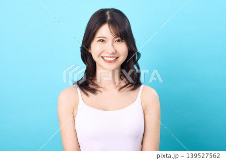 水色背景で笑顔を見せる白いキャミソール姿の若い日本人女性のポートレート 139527562