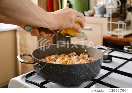 Cooking chicken in a kitchen while grating lemon for flavor 139527964