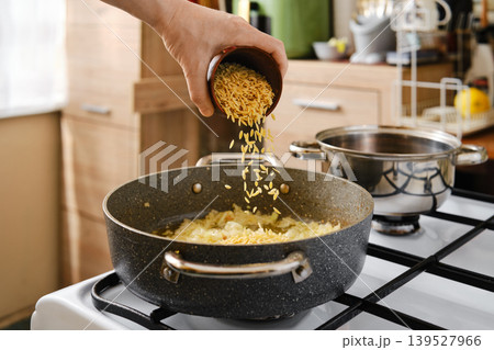 Add pasta orzo into a frying pot with chopped onion Add pasta orzo into a frying pot with chopped onion 139527966