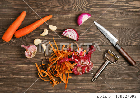 Carrots, garlic, and red onion are prepared on a wooden table with a knife and peeler Carrots, garlic, and red onion are prepared on a wooden table with a knife and peeler 139527995