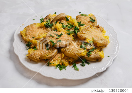 Crispy smashed potatoes served on a white plate with herbs in a kitchen setting at dinner time Crispy smashed potatoes served on a white plate with herbs in a kitchen setting at dinner time 139528004
