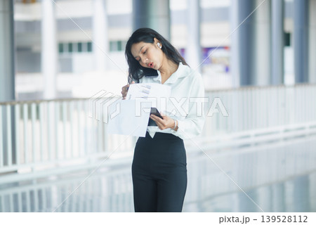 Professional businesswoman reviews financial charts on a clipboard in a modern office corridor, holding documents for corporate planning, data analysis, productivity, and business workflow concepts. Professional businesswoman reviews financial charts on a clipboard in a modern office corridor, holding documents for corporate planning, data analysis, productivity, and business workflow concepts. 139528112
