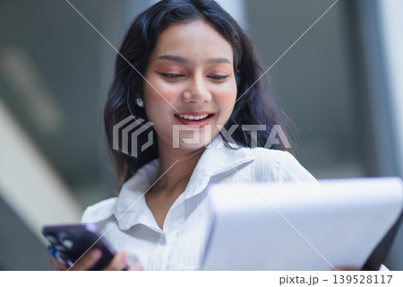 Smiling businesswoman writes on a clipboard and looks away in a bright modern office corridor, symbolizing career growth, corporate confidence, planning, leadership, and business success Smiling businesswoman writes on a clipboard and looks away in a bright modern office corridor, symbolizing career growth, corporate confidence, planning, leadership, and business success 139528117