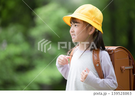 新緑の中ランドセルで走る登校する笑顔の女の子　黄色い帽子を被った1年生の新生活、学資保険などに 139528863
