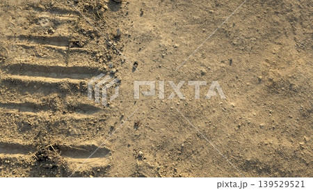 Dry brown soil features deep tractor tire tracks, scattered stones. This natural earth background captures agricultural land under warm sunlight. Perfect for farming, construction themes. 139529521