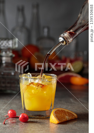 Strong alcohol is poured into a glass with ice and orange juice. Strong alcohol is poured into a glass with ice and orange juice. 139530688