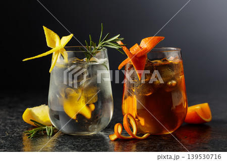 A gin and tonic and an Old Fashioned in frosted glasses on a black table. A gin and tonic and an Old Fashioned in frosted glasses on a black table. 139530716