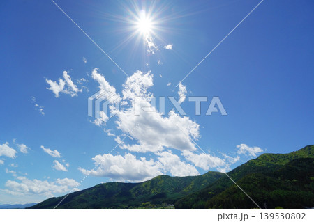 ギラギラ輝く太陽と少し雲のある爽やかな青空と山の風景 ギラギラ輝く太陽と少し雲のある爽やかな青空と山の風景 139530802