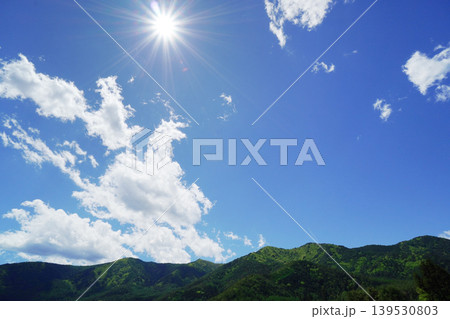 ギラギラ輝く太陽と少し雲のある爽やかな青空と山の風景 ギラギラ輝く太陽と少し雲のある爽やかな青空と山の風景 139530803