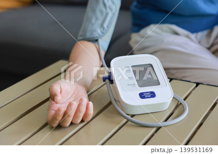 Close up shot of a person measuring blood pressure with an automatic digital monitor on a table at home. Healthcare, cardiology medical concept, monitoring hypertension and daily wellness. Close up shot of a person measuring blood pressure with an automatic digital monitor on a table at home. Healthcare, cardiology medical concept, monitoring hypertension and daily wellness. 139531169