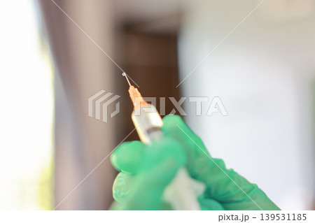 Close up macro shot of a sharp syringe needle tip with a small liquid drop. Unrecognizable doctor hand in a green latex glove preparing medicine vaccine dose for injection. Medical healthcare concept. Close up macro shot of a sharp syringe needle tip with a small liquid drop. Unrecognizable doctor hand in a green latex glove preparing medicine vaccine dose for injection. Medical healthcare concept. 139531185