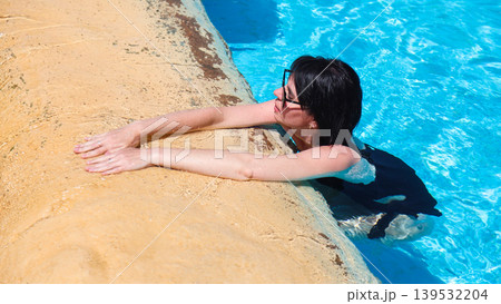 A woman rests with her hands on the edge of a pool after a long swim A woman rests with her hands on the edge of a pool after a long swim 139532204