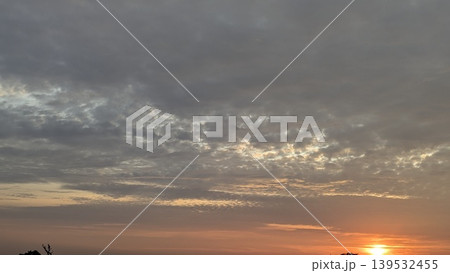 Dark textured clouds fill the dawn sky. The sun glows at the horizon, casting warm orange light. This dramatic atmospheric scene captures natural light transitions, scenic outdoor views at dawn. 139532455