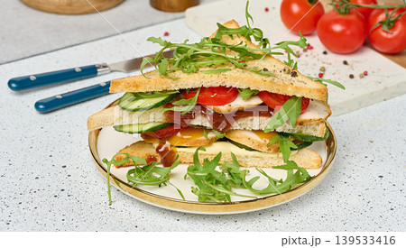Sandwich with grilled chicken, fresh cucumber, tomato, arugula and sauce on a plate, white table Sandwich with grilled chicken, fresh cucumber, tomato, arugula and sauce on a plate, white table 139533416