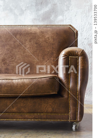 Close up of classic, vintage brown leather sofa armrest with studs. Loft interior, stucco background Close up of classic, vintage brown leather sofa armrest with studs. Loft interior, stucco background 139533700