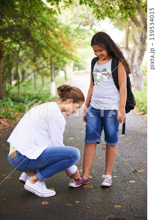 Woman, teacher and tying student shoes in park for back to school, learning or education in nature. Female person teaching little girl to tie laces on asphalt path, road or outdoor street in woods 139534015