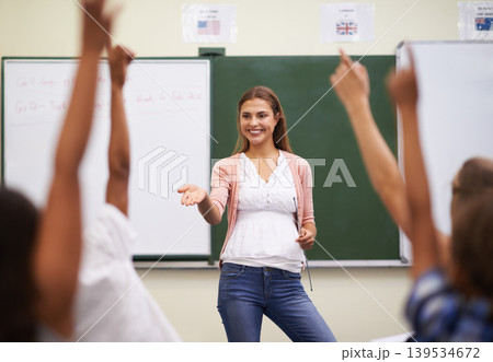 Teacher, hands and kids in classroom with question, learning and discussion for education or why. Woman, school children and happy with studying, knowledge and raised hand for scholarship or lesson 139534672