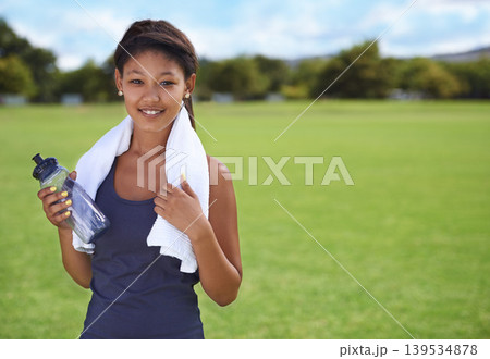 Woman, portrait and water bottle in fitness on green grass for workout, exercise or outdoor training. Face of female person or athlete with towel, drink or mineral liquid for natural sustainability 139534878