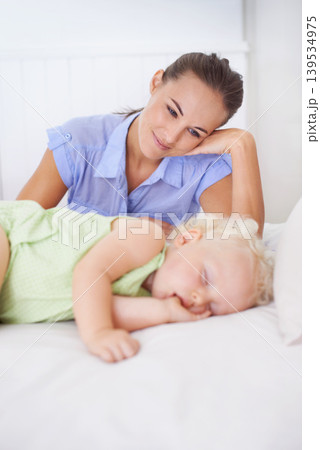 Love, sleeping and mother with baby on bed for bonding, relax and sweet cute relationship. Happy, smile and young mom watching girl child, kid or toddler taking a nap in bedroom or nursery at home. Love, sleeping and mother with baby on bed for bonding, relax and sweet cute relationship. Happy, smile and young mom watching girl child, kid or toddler taking a nap in bedroom or nursery at home. 139534975