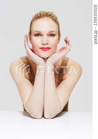 Portrait, skincare and woman in makeup at table, red lipstick and cosmetics in studio isolated on a white background. Face, beauty model and hands in spa facial treatment, wellness or healthy glow Portrait, skincare and woman in makeup at table, red lipstick and cosmetics in studio isolated on a white background. Face, beauty model and hands in spa facial treatment, wellness or healthy glow 139535028