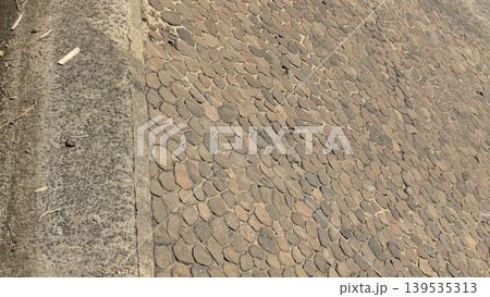 Detailed texture of stone dam wall construction, brown rock masonry surface under bright sunlight, solid outdoor infrastructure material, rural water management structure, natural stone pattern. 139535313