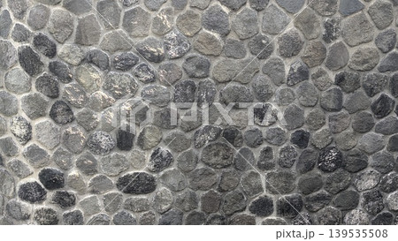 Stone wall texture with gray rocks, natural masonry pattern background, solid outdoor structure surface, detailed pebble arrangement under bright light, rural construction material backdrop. 139535508