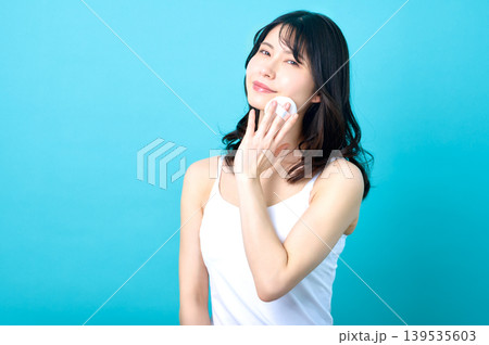 頭を傾けてパフを頬に当てる白キャミ姿の若い日本人女性 頭を傾けてパフを頬に当てる白キャミ姿の若い日本人女性 139535603