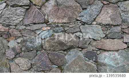 Beautiful unprocessed stonework made of solid granite boulders and small pebbles, a fragment of a wall or fence made of natural stone, the texture of the stones in the structure of the exterior finish 139535680