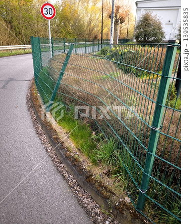 A green metal fence along an asphalt road damaged after a collision 139535835