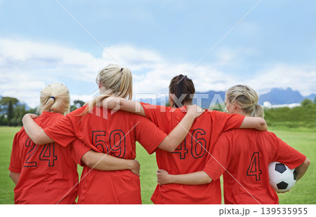 Woman, back and hug in soccer of sports team ready for match, game or outdoor practice with blue sky. Rear view of female person or group of football players standing in unity with ball in nature 139535955