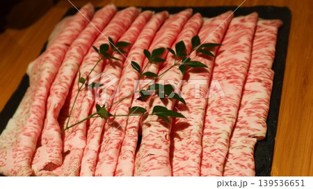 close up of Thinly sliced marbled Wagyu beef arranged in rows on dark plate with garnish sprig for sukiyaki close up of Thinly sliced marbled Wagyu beef arranged in rows on dark plate with garnish sprig for sukiyaki 139536651