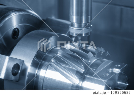 Advanced 5-axis CNC milling machine cutting a complex bevel gear shape on a transmission gear shaft. Advanced 5-axis CNC milling machine cutting a complex bevel gear shape on a transmission gear shaft. 139536685