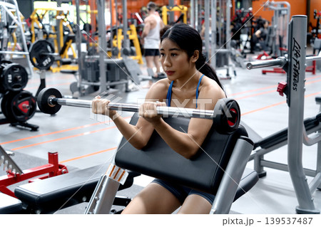 Young muscular woman exercising with dumbbells in a fitness club Young muscular woman exercising with dumbbells in a fitness club 139537487