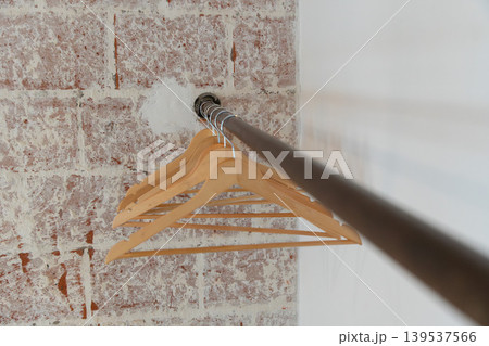 Wooden clothes hangers line metal rail against exposed brick, with shallow perspective creating clean storage detail in minimal interior. Hospitality, closet organization, retail display, interior 139537566