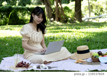 Young woman using laptop while having picnic on mat in park Young woman using laptop while having picnic on mat in park 139537604