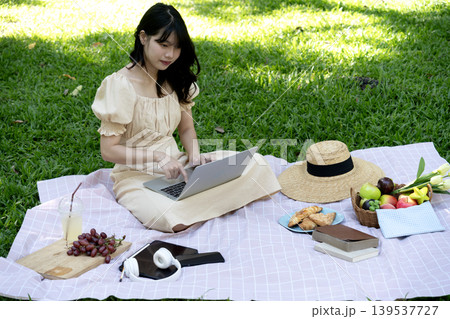 Young woman using laptop while having picnic on mat in park 139537727