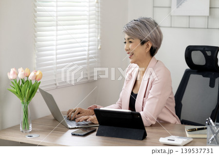 Elder businesswoman smiling while working on a laptop Elder businesswoman smiling while working on a laptop 139537731