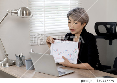 Elder Business woman is sitting at a desk with a laptop and a tablet 139537779