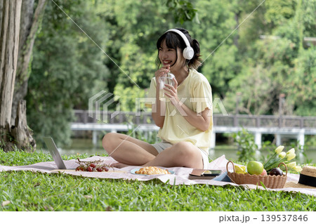 Young woman sits comfortably on a mat on a grassy lawn in a park 139537846