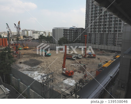 An industrial Bangkok construction site featuring a towering crane against the urban skyline with busy transport roads and concrete building architecture An industrial Bangkok construction site featuring a towering crane against the urban skyline with busy transport roads and concrete building architecture 139538046